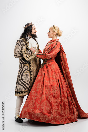 full length of historical interracial couple in crowns and medieval clothing looking at each other on white
