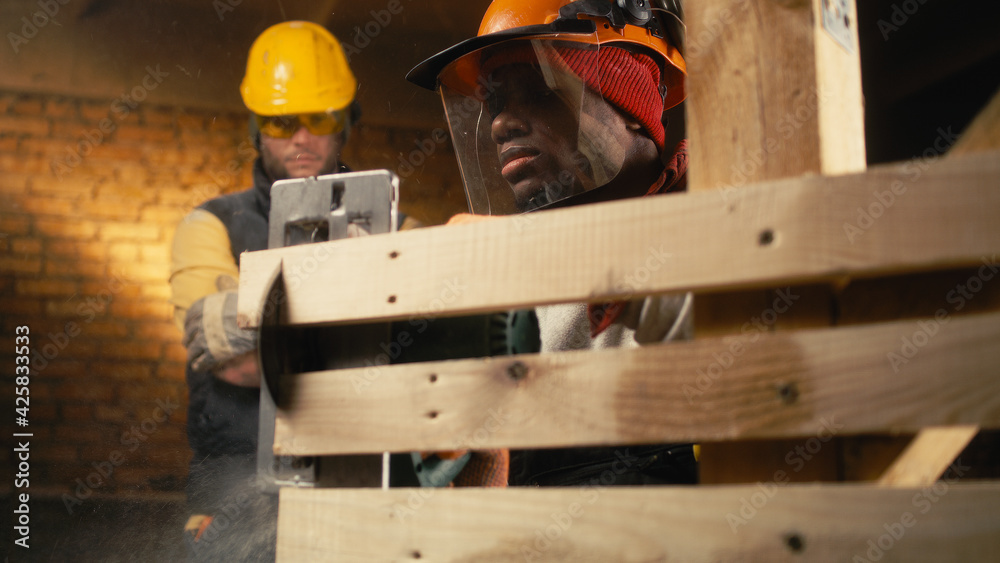 Diverse male carpenters cutting timber boards together Diverse male carpenters cutting timber boards together