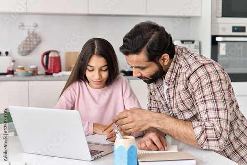 Indian dad helping school child teen daughter studying online at home. Father and kid girl elearning having virtual class on laptop, studying remote homeschool on computer, doing homework together.