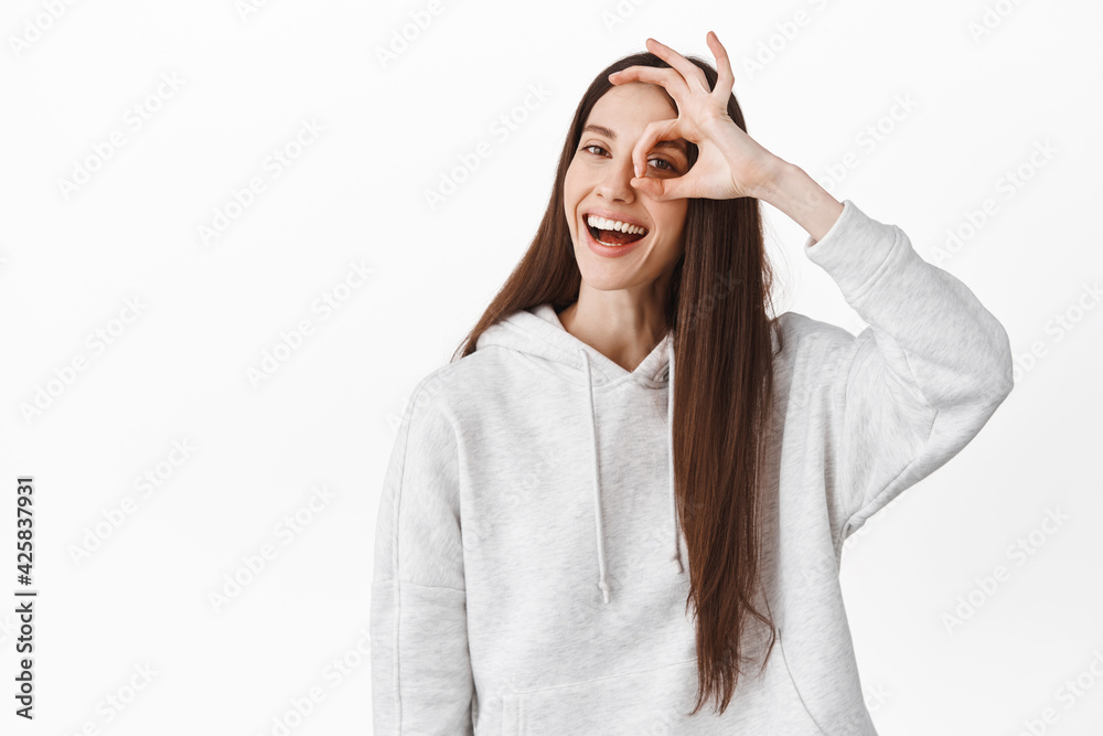 Positive young woman say yes, shows okay sign on eye and smiling, make OK agree gesture, praise perfect, excellent choice, satisfied by something good, standing over white background Positive young woman say yes, shows okay sign on eye and smiling, make OK agree gesture, praise perfect, excellent choice, satisfied by something good, standing over white background