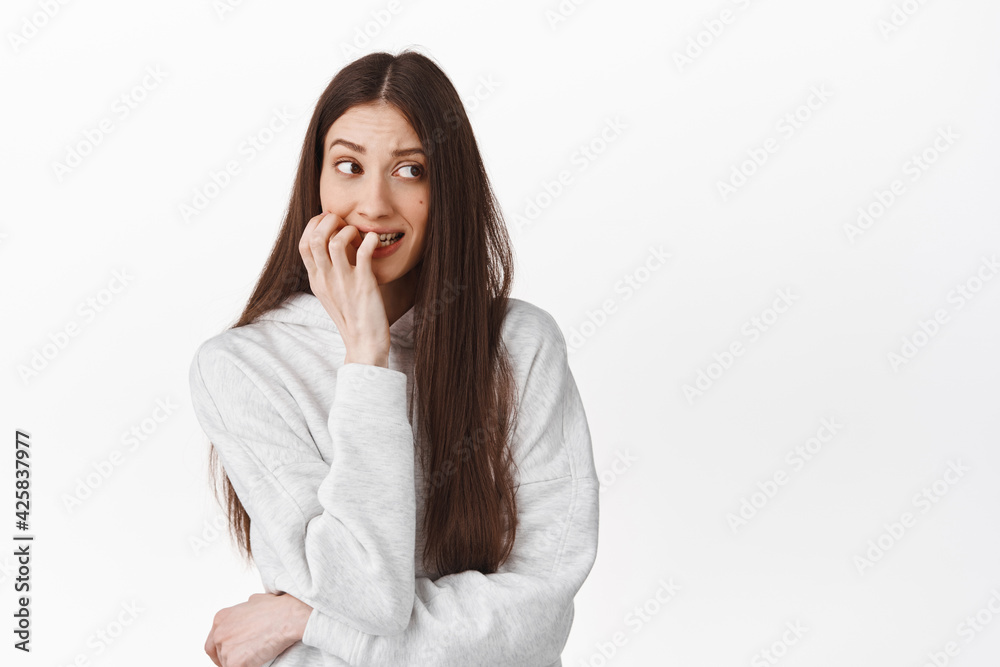 Nervous girl biting fingers and looking aside as something anxious, have anxiety, being worried, standing against white background Nervous girl biting fingers and looking aside as something anxious, have anxiety, being worried, standing against white background