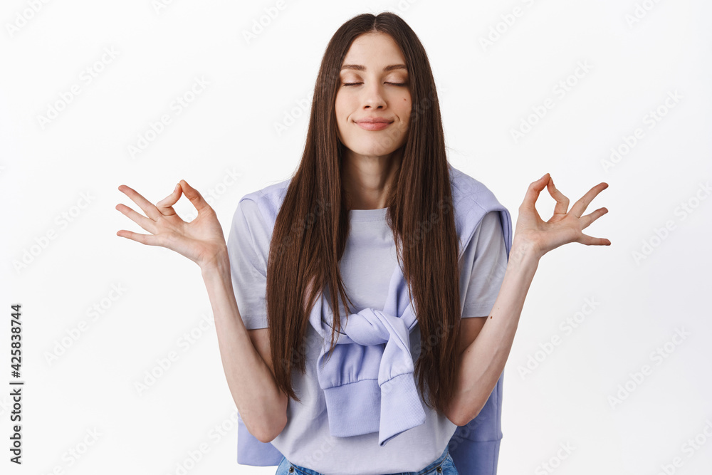 Positive thoughts only. Smiling young woman meditating, practice yoga with closed eyes, breathing calm and relaxed, resting, having peace in mind, standing over white background
