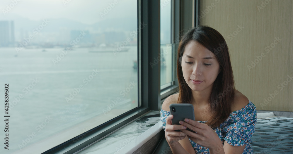 Woman use of mobile phone and sit beside window