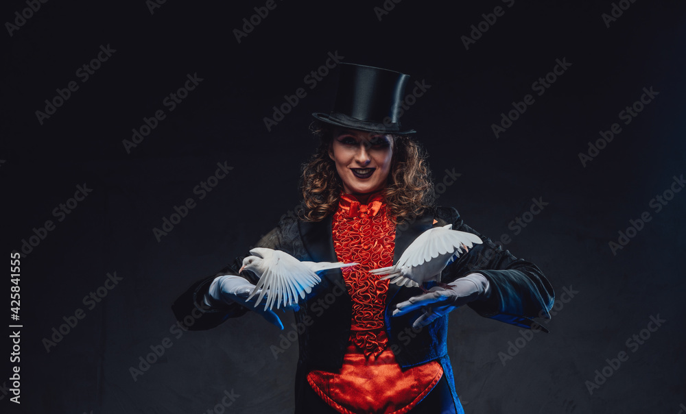 Serious female magician with white pigeons and top hat in dark background