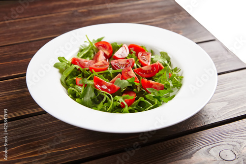 Fresh vegetable salad with tomatoes and arugula in white plate on wooden table