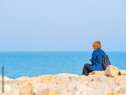 Woman sitting on a rock on the beach of the Black Sea and looking at the horizon.
