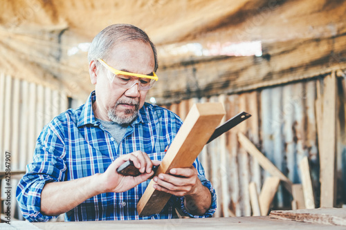 Принти на полотні Asian senior male carpenter equals a wooden bar in the workshop with wood boards background