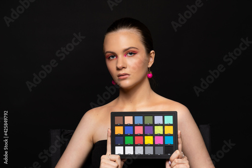Pretty woman wearing round pink earrings holding a colorchecker