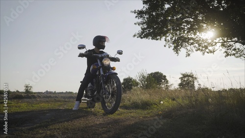 Motorcyclist standing with motorcycle on a road. Motorcyclist on a motorcycle on a background of wood at sunset