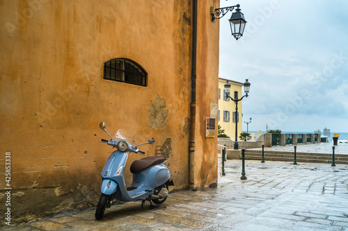 Un scooter bleu ciel dans une rue d'Ajaccio contraste avec les murs ocres jaune  des maisons dans les ruelles de la vieille ville corse. photo