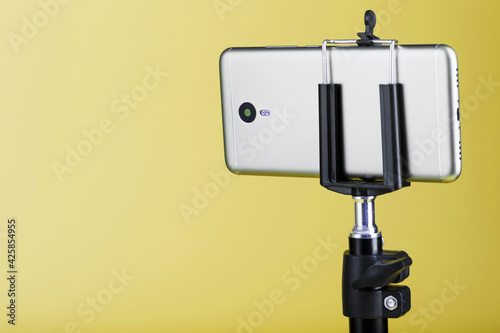 Smartphone attached to a tripod on a yellow background.