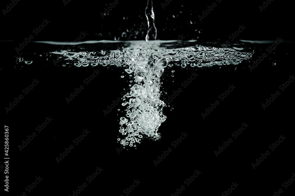 a jet of water on a black background. A splash and a bubble of air under the water.