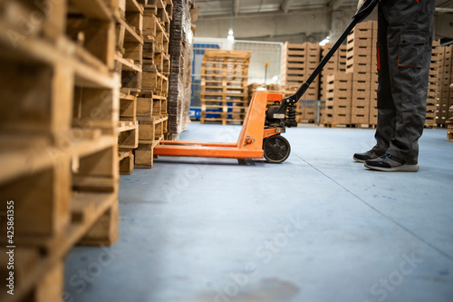 Working at warehouse. Low angle view of unrecognizable worker lifting palette with manual forklift. photo