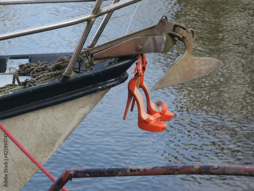 Canvas Print orange high heels hanging under an anchor on the prow of a boat