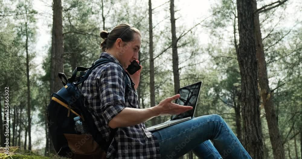Young hipster man using laptop in forest and talking on the phone, freelance working in nature, fast 5g internet connection. Young hipster man using laptop in forest and talking on the phone, freelance working in nature, fast 5g internet connection.