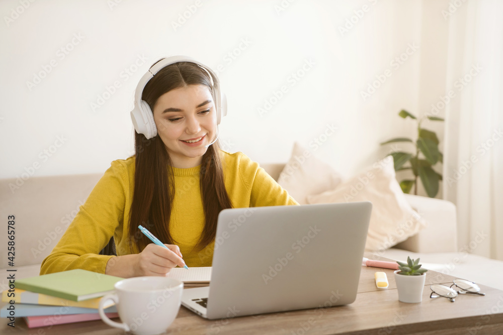 Smiling woman student in wireless headphone study online with laptop at home. Distance learning and online internet work concept. Smiling woman student in wireless headphone study online with laptop at home. Distance learning and online internet work concept.