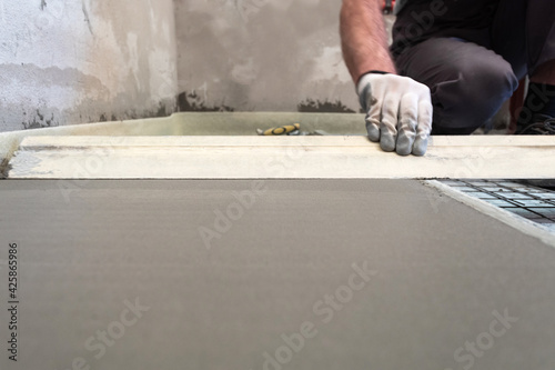 Construction worker performs floor screed indoors. Leveling the floor.