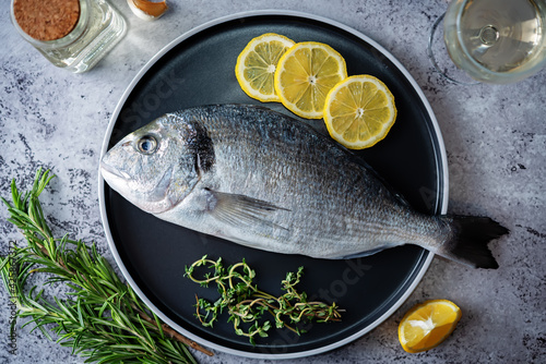 Raw fresh dorada fish with lemon slices and greens