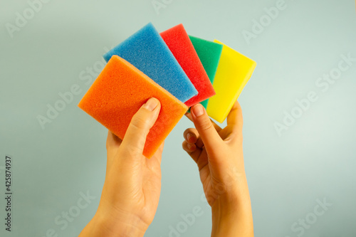 Multi-colored sponges for washing and cleaning in the hands of a woman on a blue background. Cleaning concept
