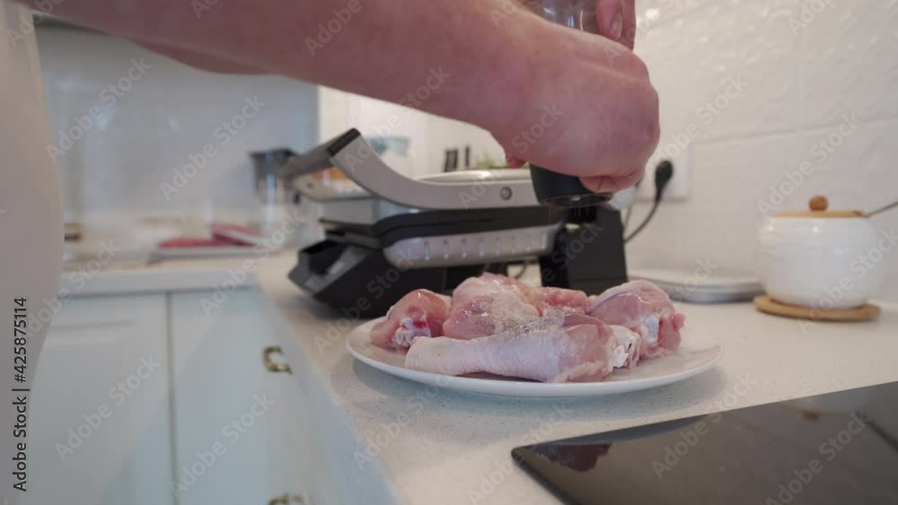 Man preparing food in the kitchen cooking chicken drumsticks in electric grill sprinkling with ground pepper, using pepper mill. High quality 4k footage Man preparing food in the kitchen cooking chicken drumsticks in electric grill sprinkling with ground pepper, using pepper mill. High quality 4k footage
