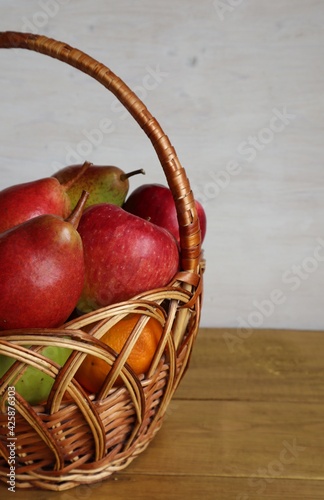 A wicker basket of fruit, apples and pears, stands on the table.	