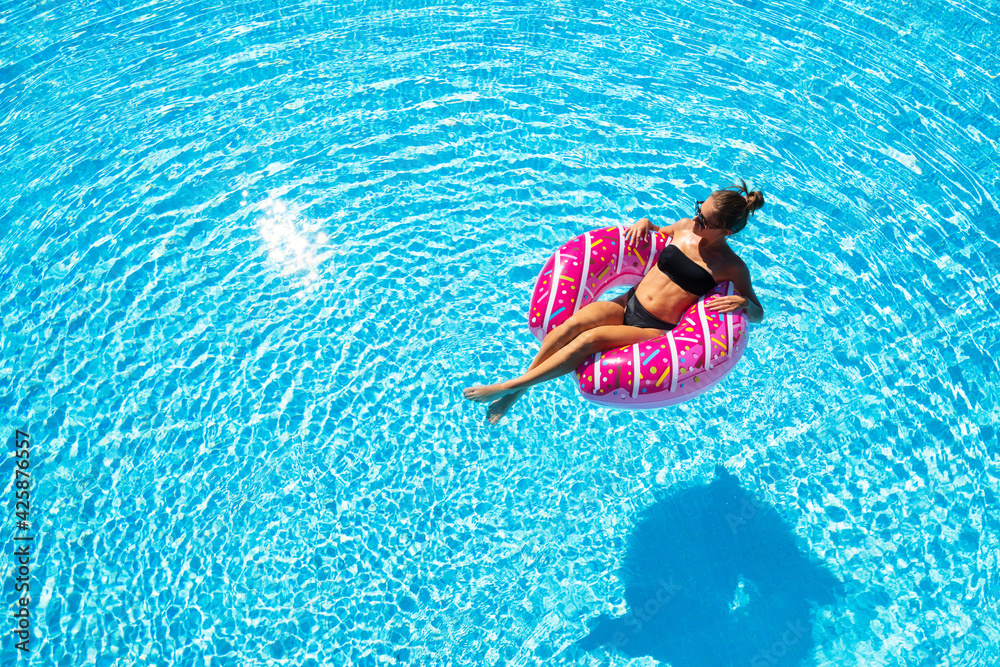 Beautiful young woman swimming on the pink donut swim ring in transparent blue water at sunset in summer. Tropical landscape with sexy slim girl in pool, clear water. Top view. Travel. Aerial view	