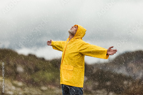 Traveler man in yellow raincoat in the clouds mountains in stormy weather with rain