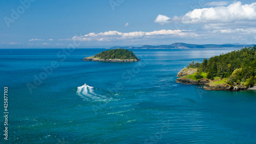 Nice cruise yacht in the Pacific Ocean over green shoreline and small island and blue sky with white clouds.