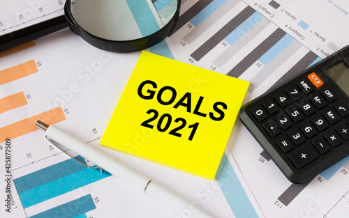 Yellow sticker with text Goals 2021 with calculator white pen magnifying glass on the diagrams