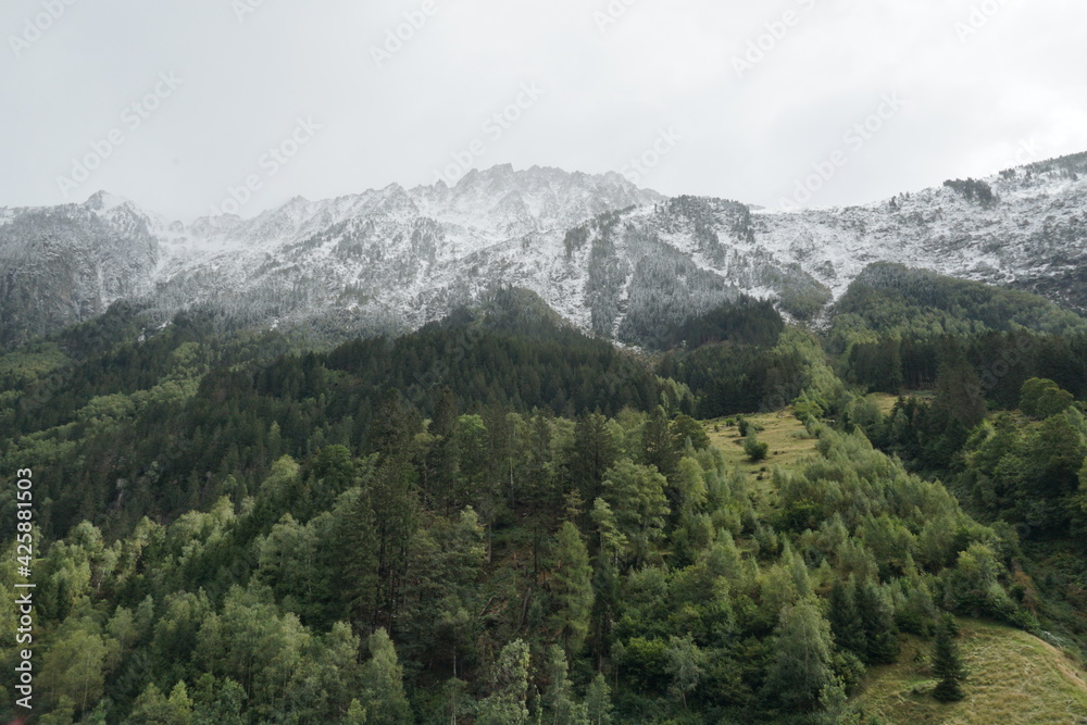 Mountainous landscape with first snow on mountain tops in late autumn at low angle view. The slopes are covered with coniferous trees in various shades of green. Area of Gotthard Pass in Switzerland.