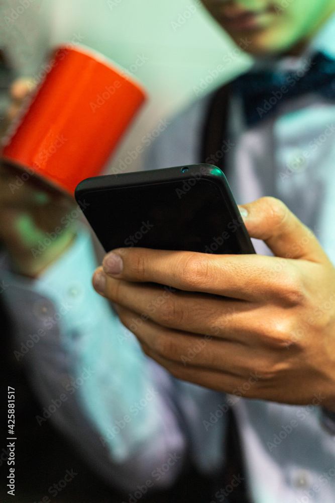 selective focus of a mobile phone used by a young man to send messages over the Internet before going to work and drinking a cup of coffee with milk