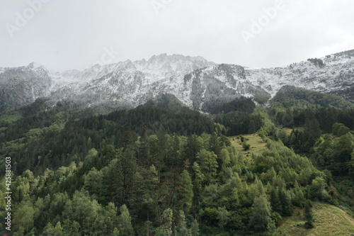 Mountainous landscape with first snow on mountain tops in late autumn at low angle view. The slopes are covered with coniferous trees in various shades of green. Area of Gotthard Pass in Switzerland.