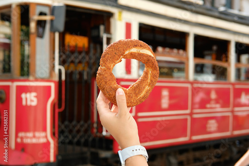 Girl holds a simit in her hand against the background of the famous red tram in Istanbul, Turkey. Traditional Istanbul simit.
