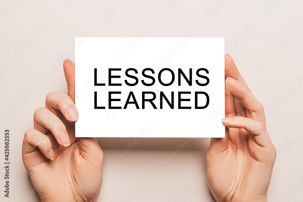 Female hands hold card paper with text LESSONS LEARNED on a yellow background. Education and study concept Female hands hold card paper with text LESSONS LEARNED on a yellow background. Education and study concept