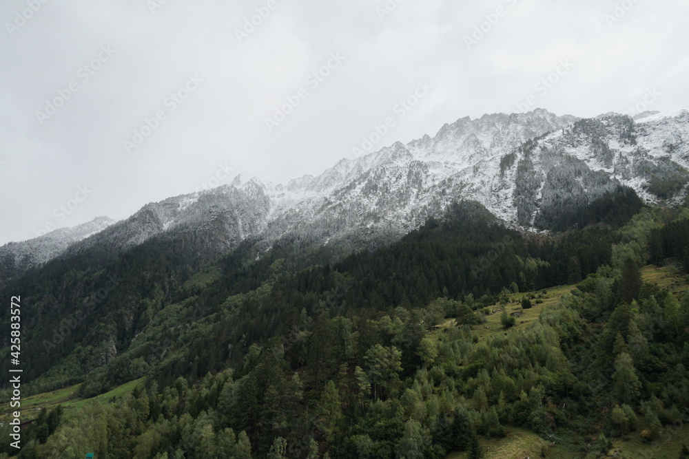 Mountainous landscape with first snow on mountain tops in late autumn with copy space. The slopes are covered with coniferous trees in various shades of green. Area of Gotthard Pass in Switzerland.
