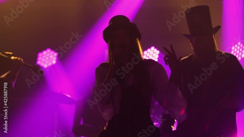 Dynamic performance of a rock band with a young female soloist in a dark smoky studio with purple lights. The band performs in Irish style clothing. Silhouette. Close up. photo