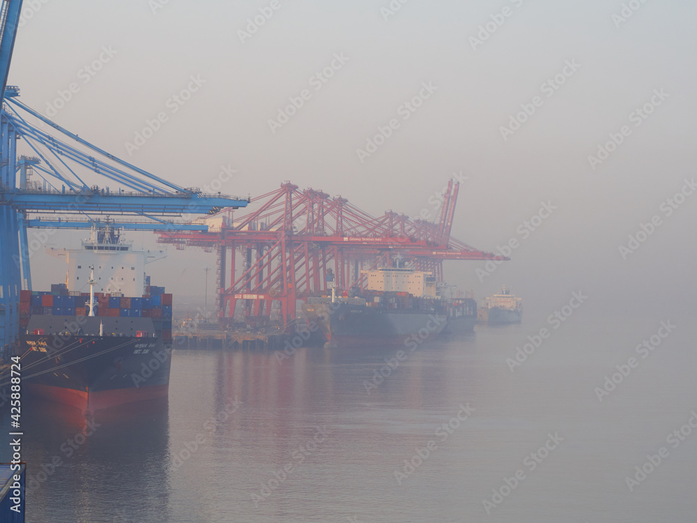 Naklejka premium India, Mumbai Port Trust - 25 January, 2017: View to moored container vessels with port cranes during the morning fog.