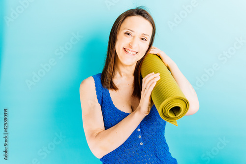 Beautiful young woman holding a yoga mat on blue background. stretching sport personal care concept
