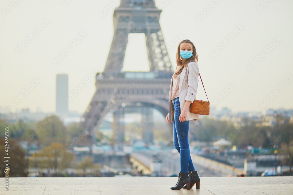 Young girl standing near the Eiffel tower in Paris and wearing protective face mask during coronavirus outbreak