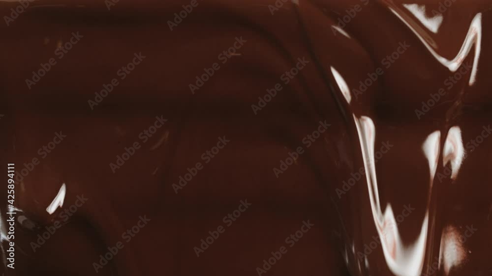 Close-up macro shot hot melted liquid chocolate flows, flowing molten chocolate or dark caramel stream. Cooking handmade chocolate dessert and candies. Confectionery. Pouring chocolate waves