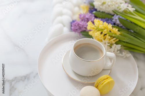 Top view composition with cup of coffee, pastry macarons and spring multicolored hyacinth on white fluffy knitted plaid