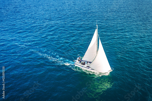 Regatta sailing ship yachts with white sails at opened sea. Aerial view of sailboat in windy condition.