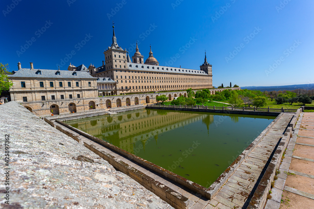El Escorial, Spain- March 17, 2021: Monastery of El Escorial. Facade with parade ground and gardens of the Escorial Monastery. Spanish Royal Palace. National Heritage. Culture of the Spanish royalty.