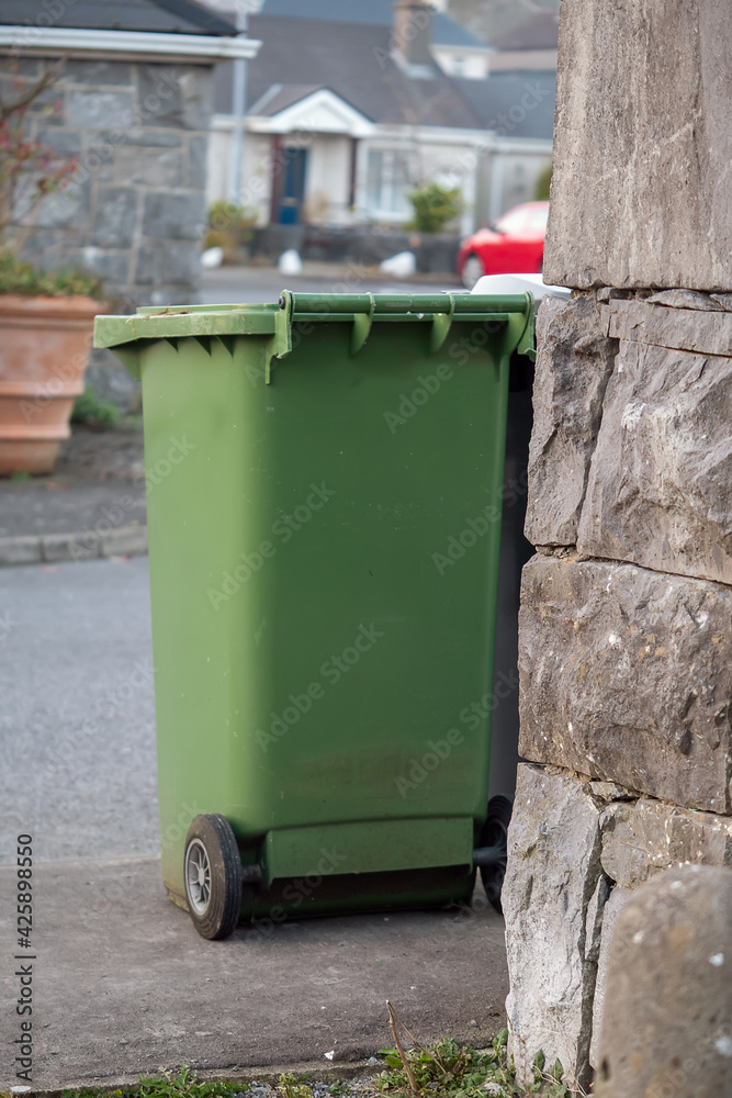 Green plastic wheelie garbage bin out in a street ready for pick up by a waste management company. Green plastic wheelie garbage bin out in a street ready for pick up by a waste management company.