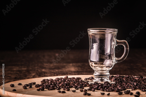 Empty cup of coffee with coffee beans around on a wooden board on a wooden table. Black background.