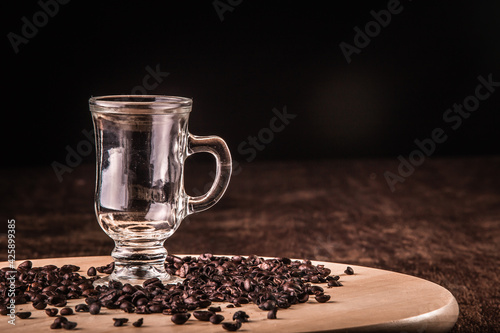 Empty cup of coffee with coffee beans around on a wooden board on a wooden table. Black background.