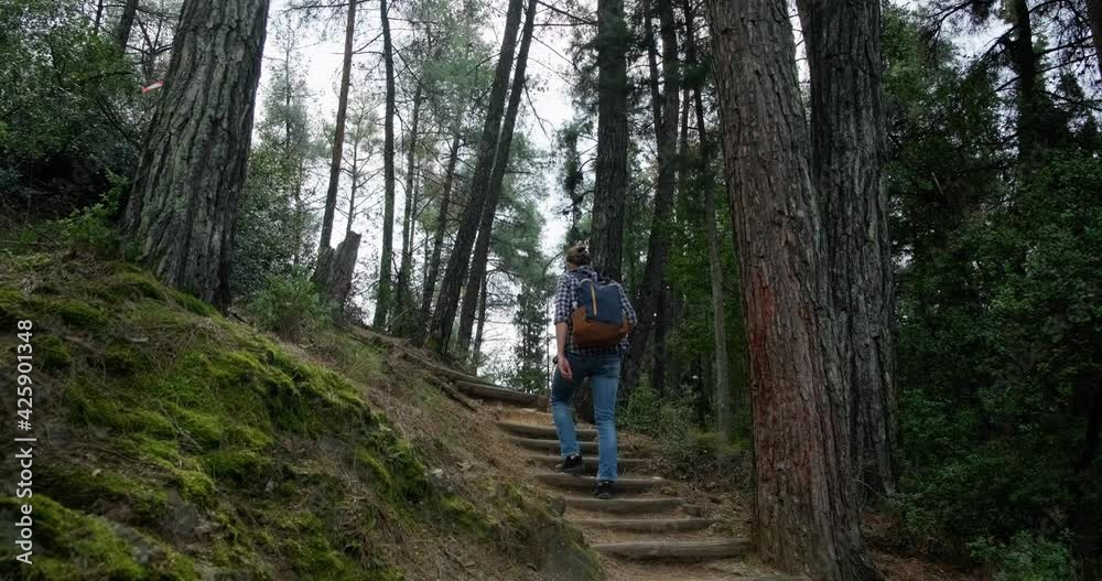 Young hipster man with hair bun and backpack hiking in the forest. Concept of digital detox, finding inner balance. Young hipster man with hair bun and backpack hiking in the forest. Concept of digital detox, finding inner balance.