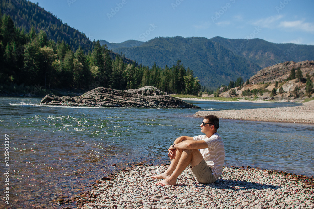 A young man walks along a mountain river in the forest.Beautiful landscape with mountains,forest,and river with large rocks on a sunny summer day.Rest Area, I-90, Alberton, Montana, USA