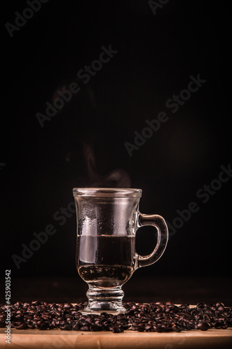 Cup of coffee with coffee beans around on a wooden board on a wooden table. Black background. Space for text.