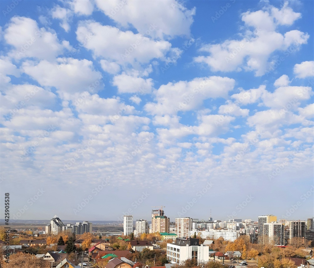 Photo of an autumn cityscape with high-rise buildings and small houses and a large sky with clouds